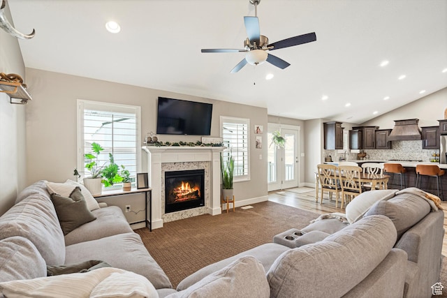 living room with a ceiling fan, a glass covered fireplace, recessed lighting, baseboards, and vaulted ceiling