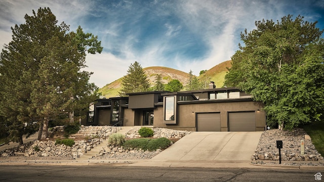 view of front of house featuring driveway, a chimney, an attached garage, a mountain view, and stucco siding