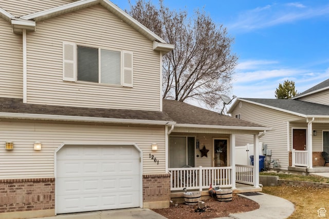 view of front facade featuring an attached garage, a porch, a shingled roof, and brick siding