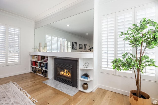living room with crown molding, plenty of natural light, a fireplace with flush hearth, and wood finished floors