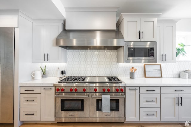 kitchen with stainless steel appliances, wall chimney exhaust hood, backsplash, and white cabinetry