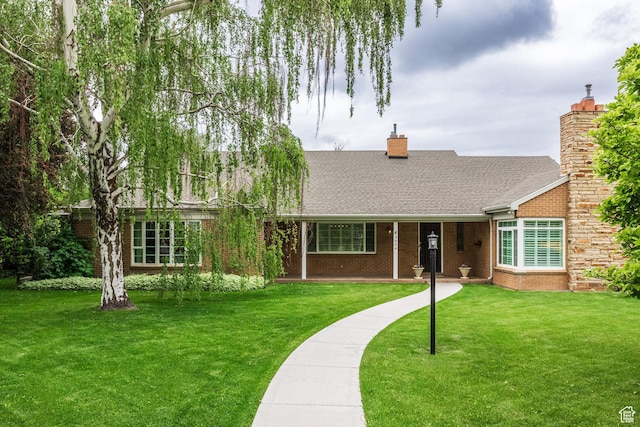 view of front of property featuring a front lawn, a shingled roof, a chimney, and brick siding