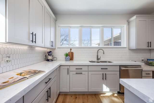 kitchen with a sink, dishwasher, decorative backsplash, and light wood-style floors