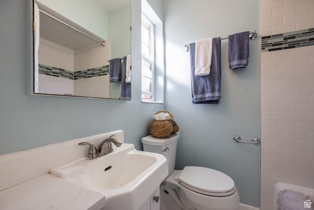 bathroom featuring a sink, toilet, and a tile shower