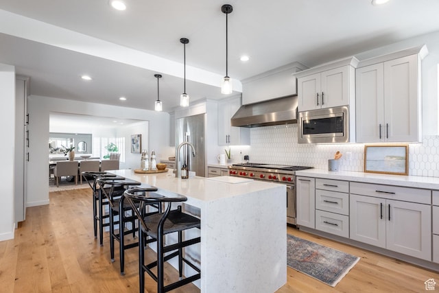 kitchen featuring high quality appliances, wall chimney range hood, a kitchen bar, tasteful backsplash, and recessed lighting