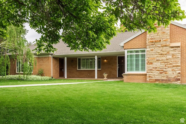 view of front of home with a front yard, roof with shingles, and brick siding