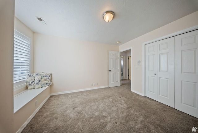 unfurnished bedroom with visible vents, a textured ceiling, a closet, carpet flooring, and baseboards