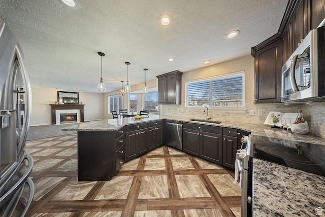 kitchen with a peninsula, stainless steel appliances, open floor plan, a glass covered fireplace, and tasteful backsplash