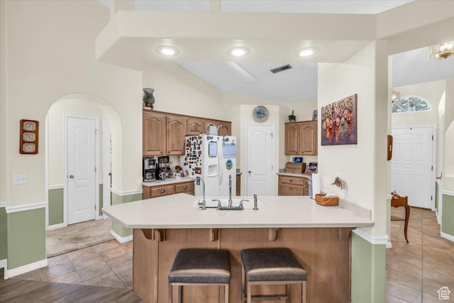 kitchen with white fridge with ice dispenser, light countertops, visible vents, and a breakfast bar area