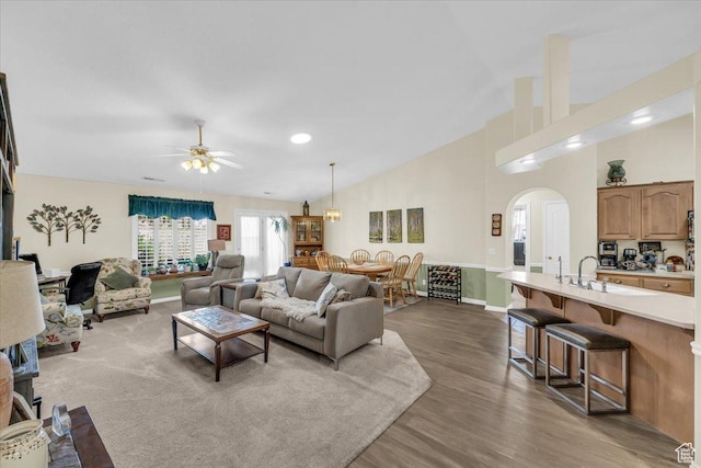 living room with arched walkways, high vaulted ceiling, dark wood-style flooring, a ceiling fan, and baseboards