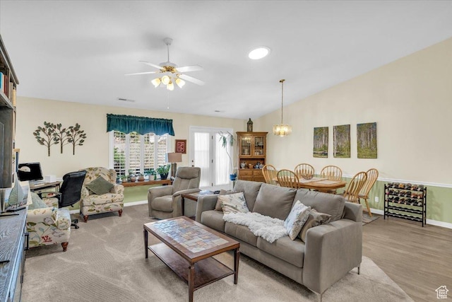 living area with visible vents, vaulted ceiling, wood finished floors, baseboards, and ceiling fan with notable chandelier