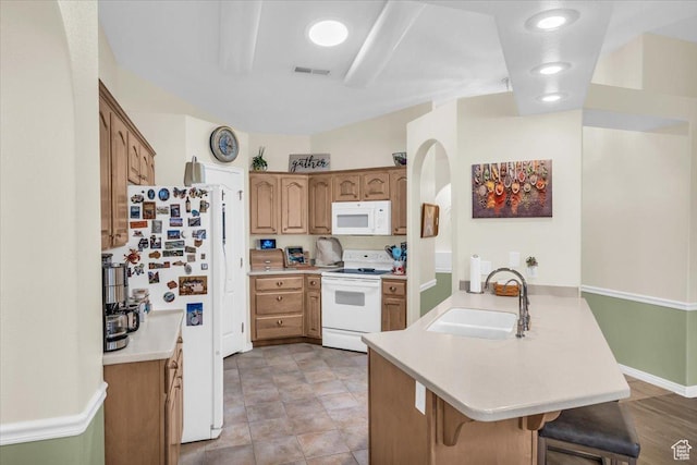 kitchen featuring a breakfast bar area, a peninsula, white appliances, a sink, and light countertops
