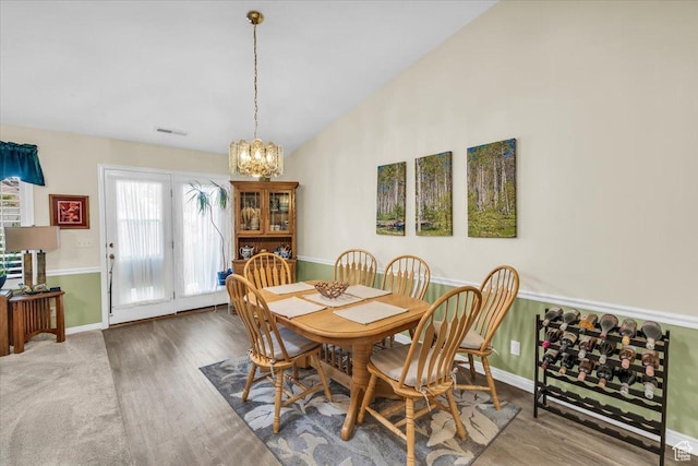 dining room featuring lofted ceiling, wood finished floors, visible vents, and a notable chandelier