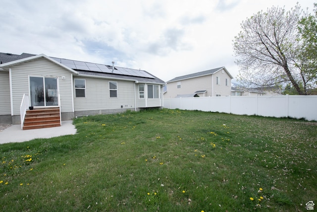 back of property featuring roof mounted solar panels, a yard, entry steps, and fence