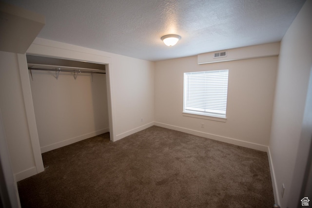 unfurnished bedroom with dark colored carpet, a textured ceiling, baseboards, visible vents, and a closet