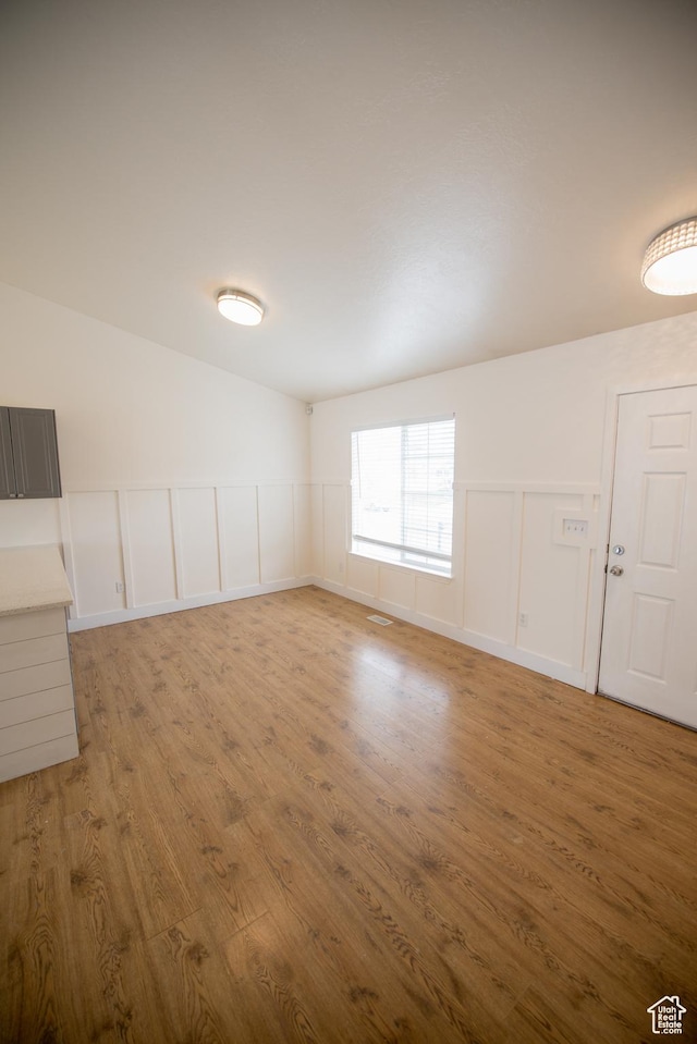 unfurnished room featuring light wood-style flooring, a decorative wall, and wainscoting