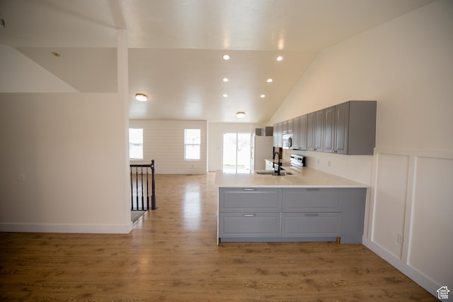 kitchen with a sink, stainless steel microwave, light wood-type flooring, gray cabinetry, and a peninsula