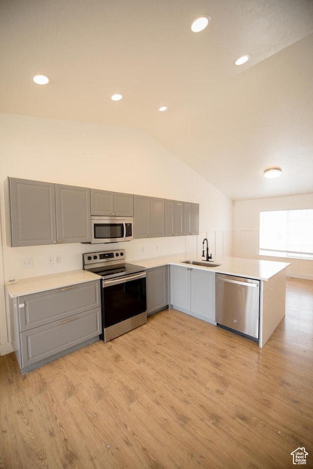 kitchen featuring lofted ceiling, gray cabinets, a sink, light wood-type flooring, and appliances with stainless steel finishes