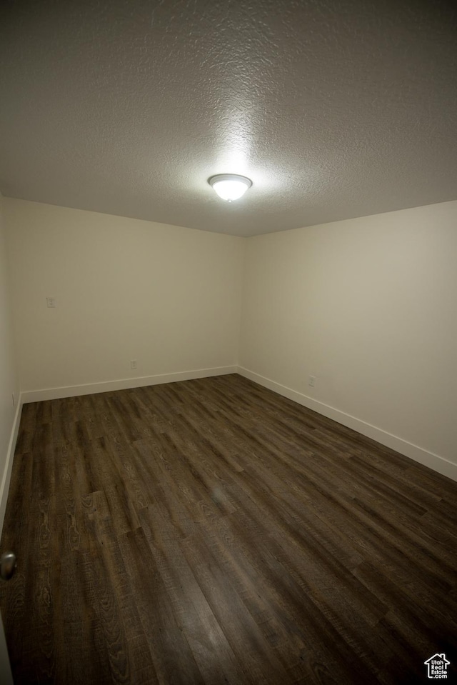 spare room featuring dark wood finished floors, a textured ceiling, and baseboards