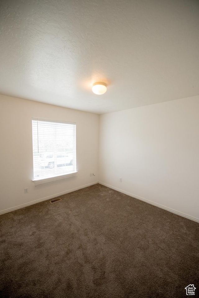 empty room featuring dark carpet, visible vents, and baseboards