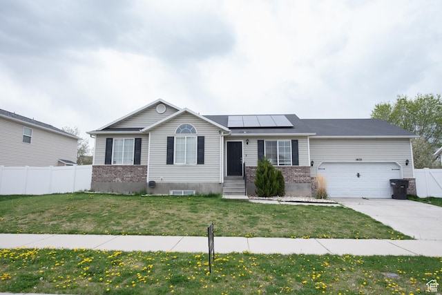 single story home featuring solar panels, driveway, fence, brick siding, and a front yard