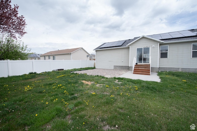 back of house featuring solar panels, fence, a yard, and entry steps