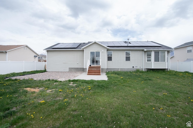 rear view of property with roof mounted solar panels, fence, entry steps, and a yard