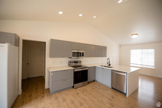 kitchen featuring stainless steel appliances, vaulted ceiling, gray cabinets, a sink, and a peninsula