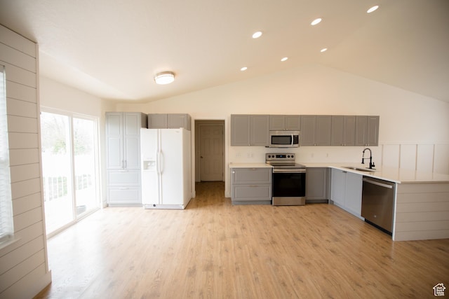 kitchen featuring vaulted ceiling, a sink, light wood-style floors, gray cabinets, and appliances with stainless steel finishes