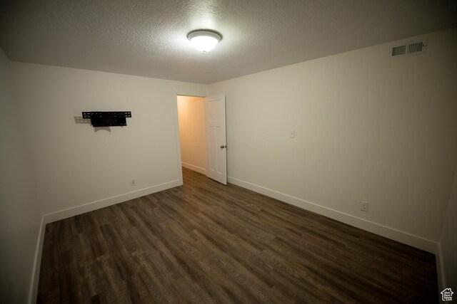 spare room featuring dark wood-type flooring, a textured ceiling, visible vents, and baseboards