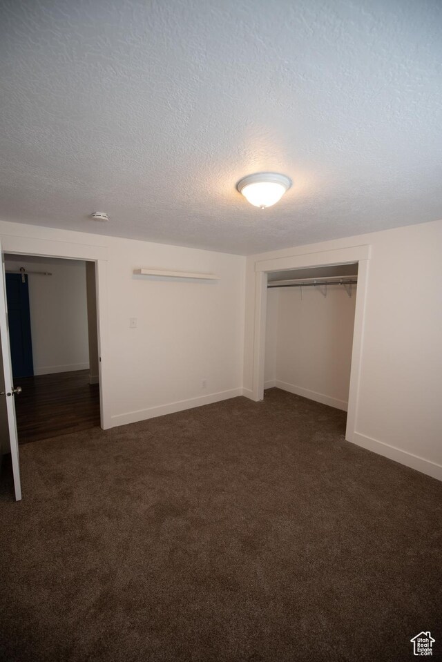 unfurnished bedroom featuring a closet, dark colored carpet, a textured ceiling, and baseboards