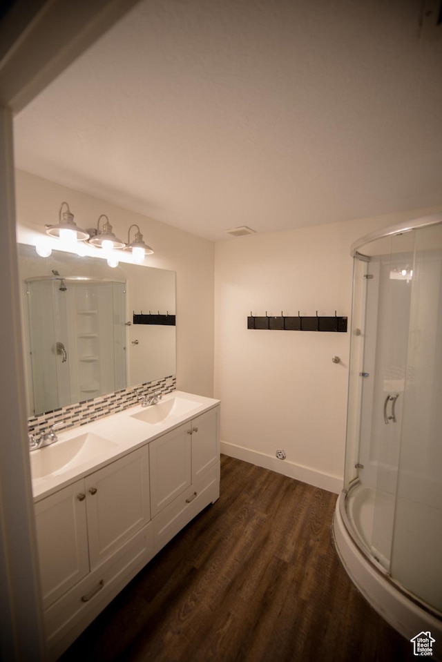 full bath featuring wood finished floors, a sink, a shower stall, and double vanity