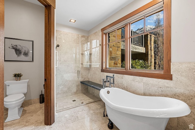 bathroom with a freestanding tub, toilet, tile walls, and a stall shower