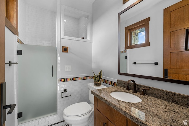 bathroom with toilet, vanity, wainscoting, a stall shower, and tile walls
