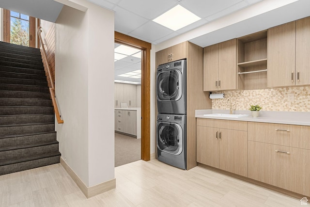 clothes washing area with a sink, baseboards, and stacked washer and clothes dryer