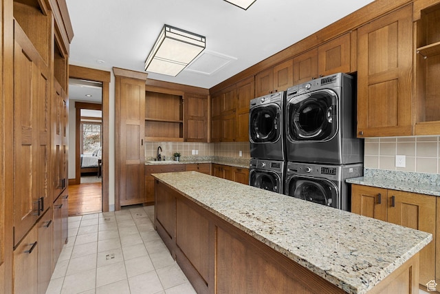 kitchen with open shelves, brown cabinetry, stacked washer and clothes dryer, and backsplash