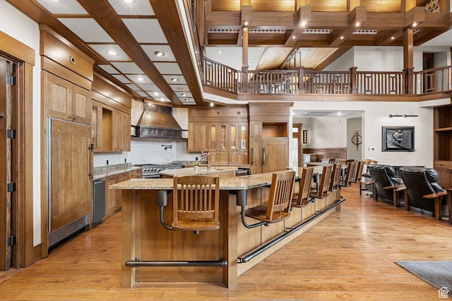 kitchen with backsplash, light wood-type flooring, custom range hood, light stone counters, and stainless steel gas stove
