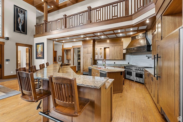 kitchen with double oven range, a spacious island, a high ceiling, custom range hood, and light wood-type flooring