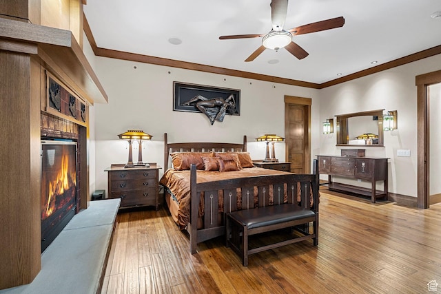 bedroom featuring a glass covered fireplace, crown molding, baseboards, and wood-type flooring