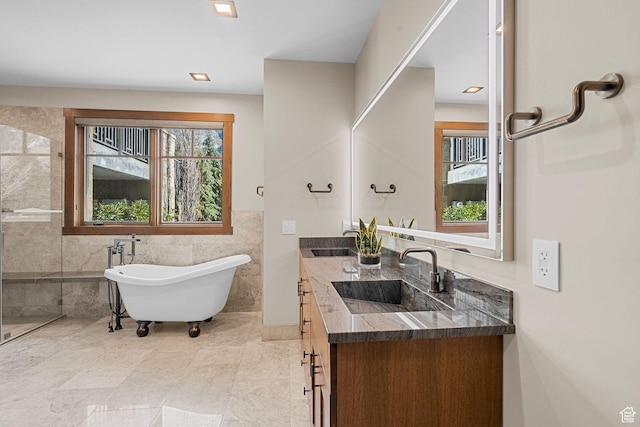 full bathroom featuring a soaking tub, plenty of natural light, tile walls, and a sink