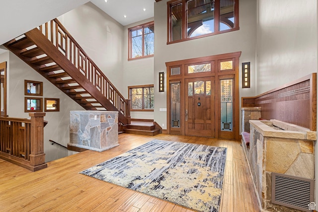 entryway with visible vents, wood-type flooring, a towering ceiling, and stairs