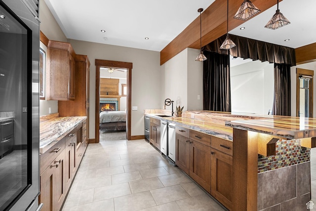 kitchen featuring stainless steel fridge, a warm lit fireplace, brown cabinetry, and light stone countertops