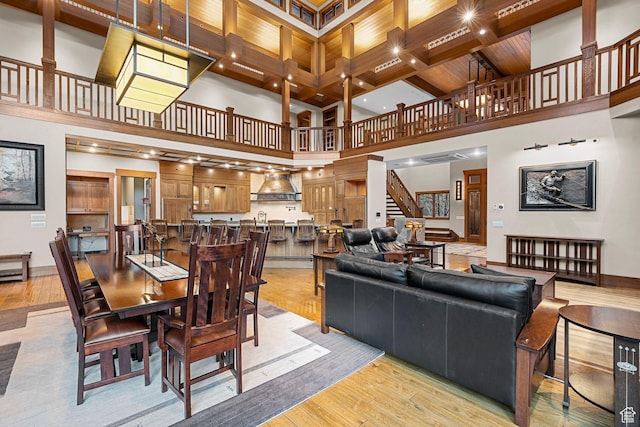 dining room with stairway, coffered ceiling, light wood finished floors, beam ceiling, and a high ceiling