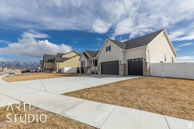 view of front facade with stucco siding, fence, a mountain view, concrete driveway, and an attached garage