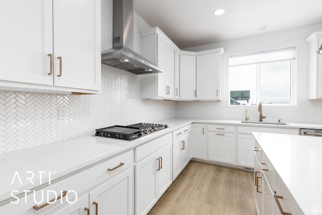 kitchen with a sink, white cabinetry, wall chimney exhaust hood, light countertops, and stainless steel gas cooktop