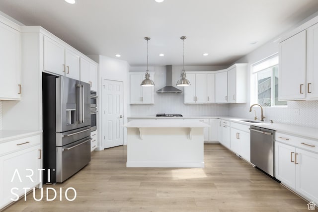 kitchen with a center island, light wood-style floors, stainless steel appliances, wall chimney exhaust hood, and a sink