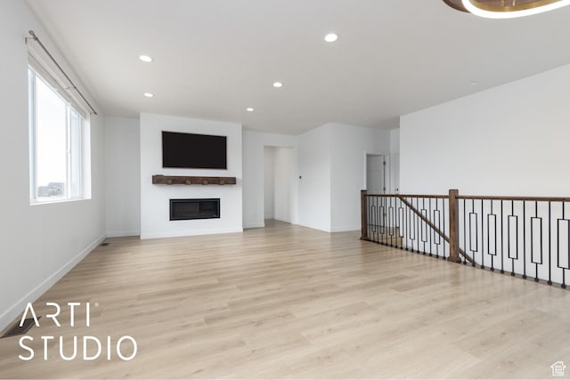 unfurnished living room featuring a glass covered fireplace, recessed lighting, baseboards, and light wood finished floors