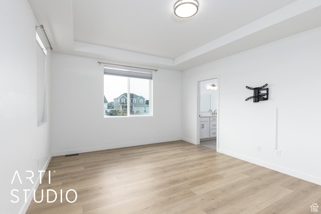 empty room featuring baseboards, light wood-type flooring, and a tray ceiling