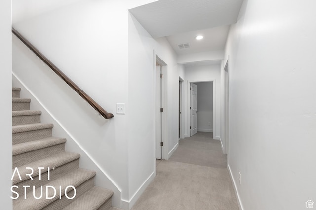 hall with visible vents, baseboards, light colored carpet, and stairs