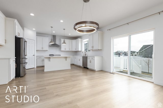 kitchen with a kitchen island, a sink, stainless steel appliances, light countertops, and wall chimney exhaust hood